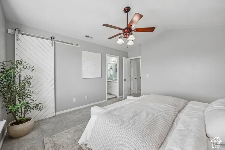 Vaulted ceilings, sliding chevron-patterned barn door, ceiling fan with integrated lighting, and neutral wall tones