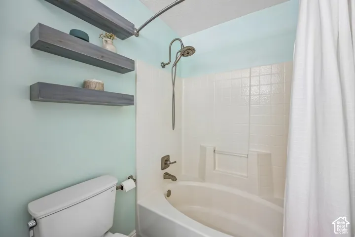 Bathtub and shower combination with a tiled surround, metallic wall-mounted showerhead and faucet, and two dark wood-finish floating shelves