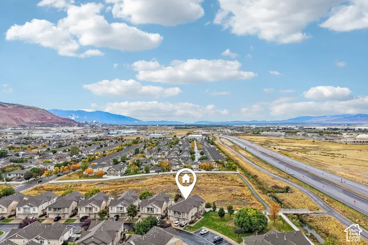 Aerial perspective featuring a multi-story residence with an attached garage, positioned on a corner lot with an expansive rear lawn and mountain scenery