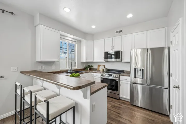 Kitchen featuring white cabinetry, wood-finish flooring, stainless steel appliances, and a breakfast bar with stone-finish countertops