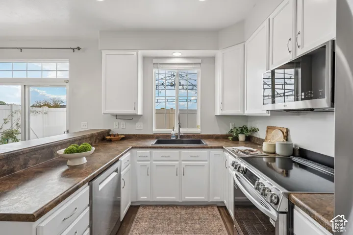 Kitchen featuring white shaker-style cabinetry, a breakfast bar, dark composite sink, stone-finish laminate countertops, and stainless steel appliances
