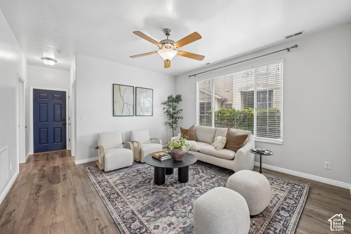 Living area featuring wood-finish flooring, a ceiling fan with integrated lighting, and a large window with horizontal blinds