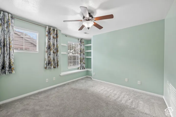 Interior room featuring carpeted flooring, a ceiling fan with integrated lighting, built-in corner shelving, and a window seat
