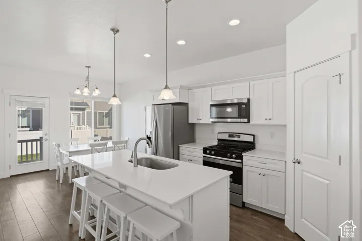 Kitchen featuring white cabinetry, stainless steel appliances, a center island with sink, pendant lighting, and wood-finish flooring