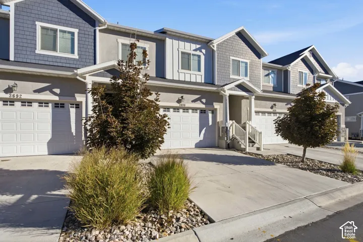 Multi-story exterior with a mix of stucco and shingle siding, individual garage doors, paved driveways, and landscaped rock beds with plantings