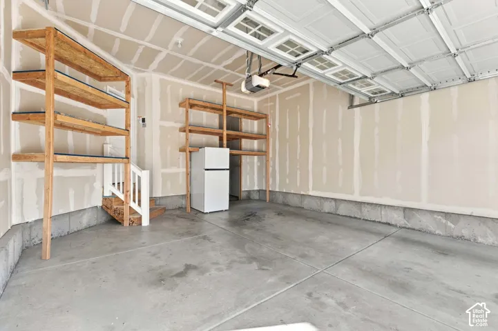 Concrete flooring with two sets of built-in wood shelving units, a built-in staircase, and an overhead garage door