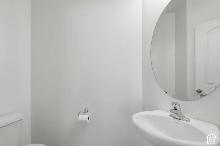 Pedestal sink with chrome faucet, oval mirror, and white toilet