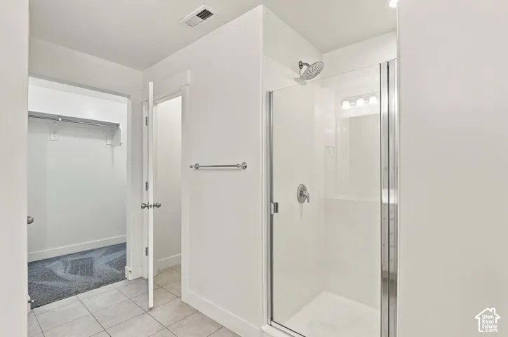 Primary Bath White-tiled flooring with a glass-enclosed shower, featuring a single-handle shower fixture and a separate walk-in closet with carpeted flooring