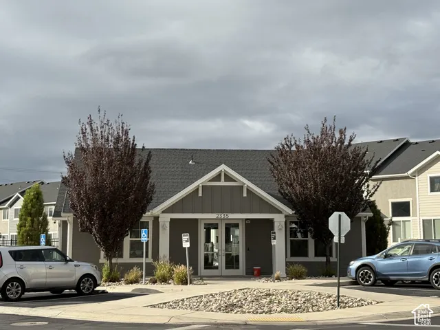 Exterior featuring horizontal siding, a gabled roofline with decorative timber brackets, double glass entry doors, and a stone-accented landscape bed