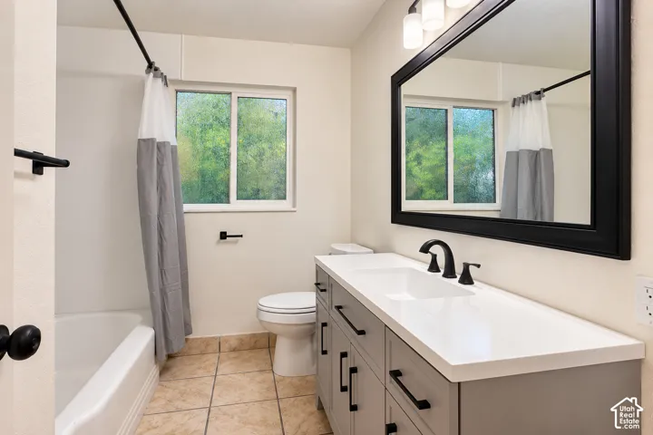 Bathroom featuring a vanity with grey cabinetry, a solid-surface white countertop, a black-framed mirror, and a tile floor