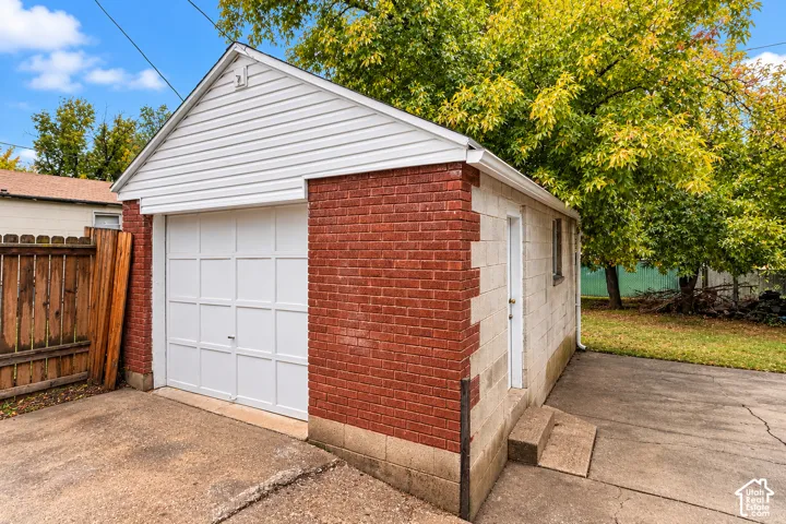 Detached garage featuring red brick and concrete block construction, white vinyl siding, a paneled garage door, and a concrete driveway