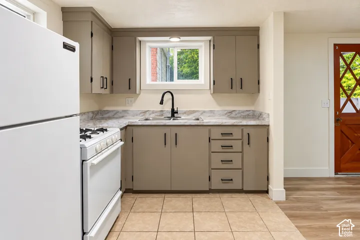Kitchen featuring neutral-toned cabinetry, stone-finish countertops, a dual-basin sink with a matte black faucet, ceramic tile flooring, and a solid wood door with decorative glass panes
