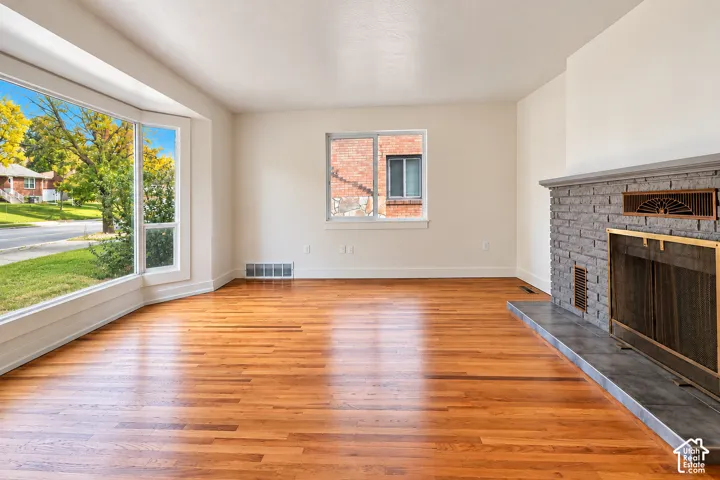 Living space featuring wood-finish flooring, a masonry fireplace with a metal screen and stone-tile hearth, and a large bay window