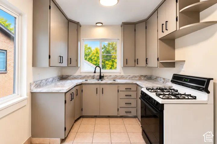 Kitchen featuring neutral-toned cabinetry with matte black hardware, stone-patterned laminate countertops, tile flooring, and a double-basin sink with a gooseneck faucet