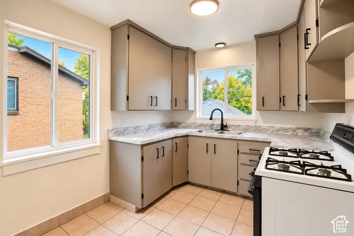 Kitchen featuring neutral-toned cabinetry, patterned laminate countertops, a dual-basin stainless steel sink with a matte black faucet, and ceramic tile flooring