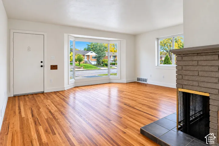Room featuring wood-finish flooring, a brick fireplace with a tile hearth, a large bay window, and neutral wall tones