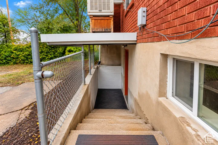 Exterior staircase featuring masonry steps, a metal chain-link perimeter fence, red brick facade, and a covered entry