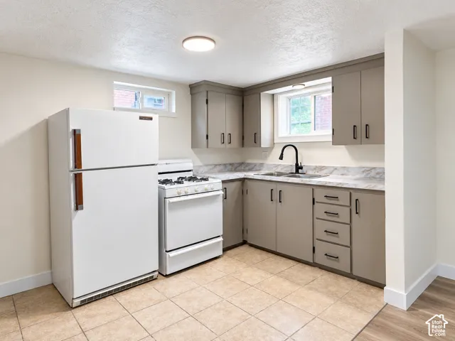 Kitchen featuring grey shaker-style cabinetry, stone-patterned laminate countertops, dual-basin sink with matte black faucet, and white appliances