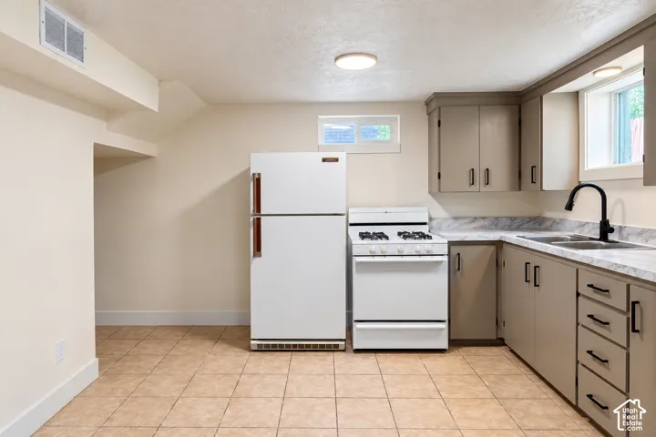 Kitchen featuring cabinetry with matte black hardware, stone-patterned laminate countertops, a dual-basin sink with a matte black gooseneck faucet, a white gas range, and tile flooring