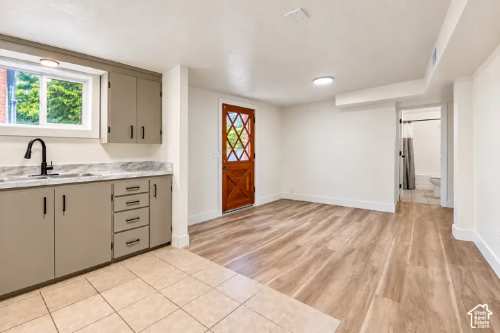 Kitchenette featuring light grey shaker-style cabinetry, stone-patterned countertops, a matte black faucet, wood-finish flooring, and a stained wood exterior door with diamond-pattern glass detailing