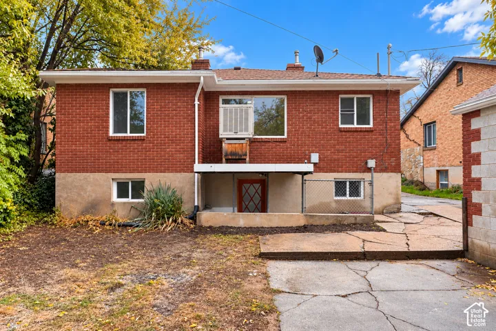 Exterior featuring red brick masonry, a concrete foundation, a paved hardscape area, and a metal chain-link perimeter fence