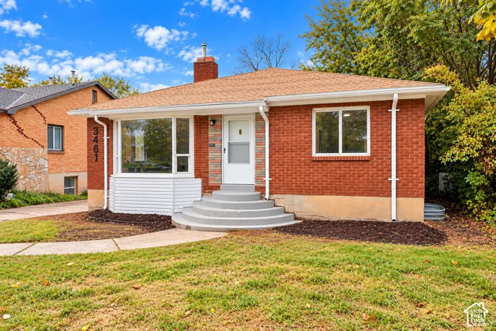 Red brick exterior featuring a multi-pane bay window, elevated concrete entry steps, a brick chimney, and a concrete front walkway
