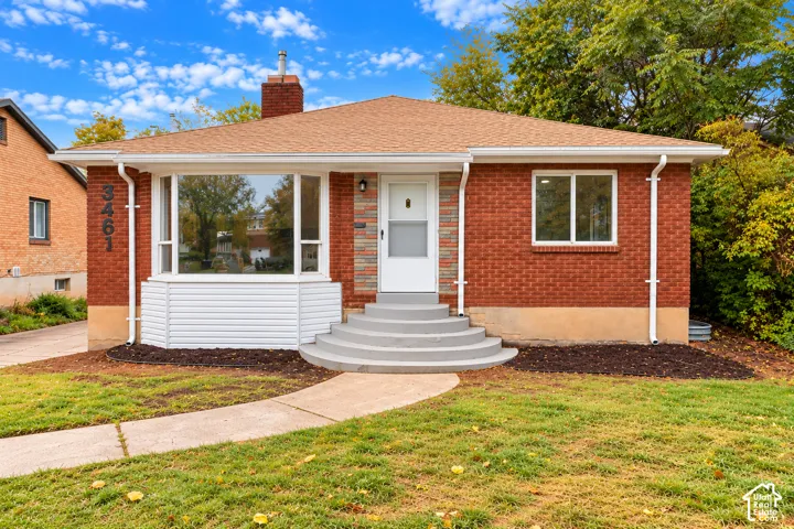 Red brick exterior featuring a bay window, concrete front steps, a central chimney, and a paved walkway