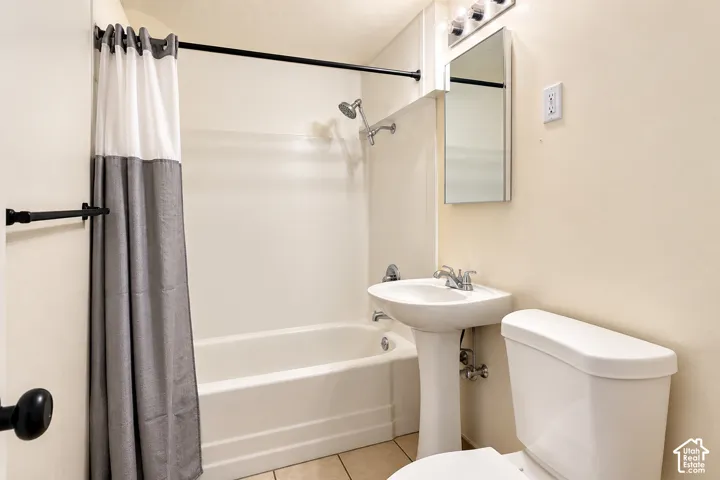Bathroom featuring a pedestal sink, a shower-tub combination with a wall-mounted showerhead, a rectangular mirror, and tile flooring