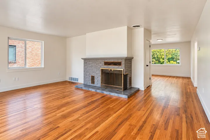 Hardwood flooring throughout featuring a brick fireplace with a tile hearth and metal fireplace screen