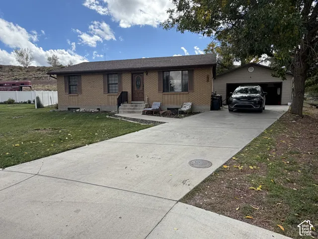 Brick exterior residence featuring a composition shingle roof, concrete driveway, detached garage, and white vinyl perimeter fencing