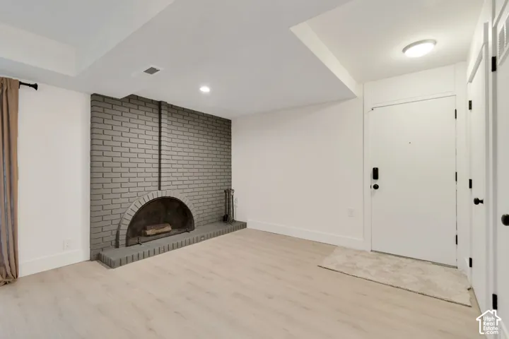 Interior space featuring wood-finish flooring, a painted brick fireplace with an arched hearth, flush-mount ceiling lighting, and solid-panel doors