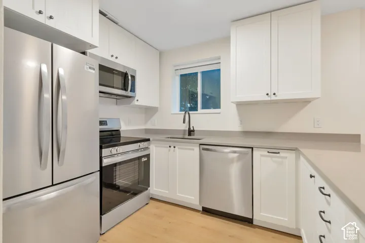 Kitchen featuring white Shaker-style cabinetry, stainless steel appliances, quartz countertops, a matte black faucet, and wood-finish flooring