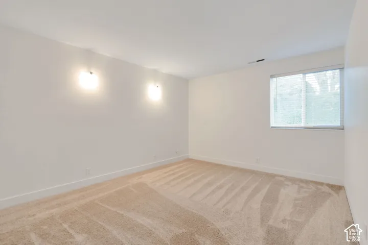 Neutral-toned wall-to-wall carpeting, dual wall-mounted light fixtures, and a window with horizontal blinds