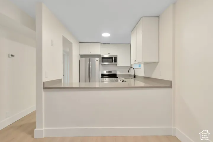 Kitchen featuring white shaker-style cabinetry, solid-surface countertops, stainless steel appliances, a matte black faucet, and wood-finish flooring
