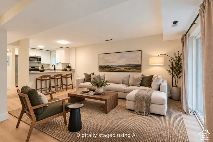 Open-concept area featuring light wood-finish flooring, white cabinetry, a breakfast bar with stone-style countertops, and sliding glass doors