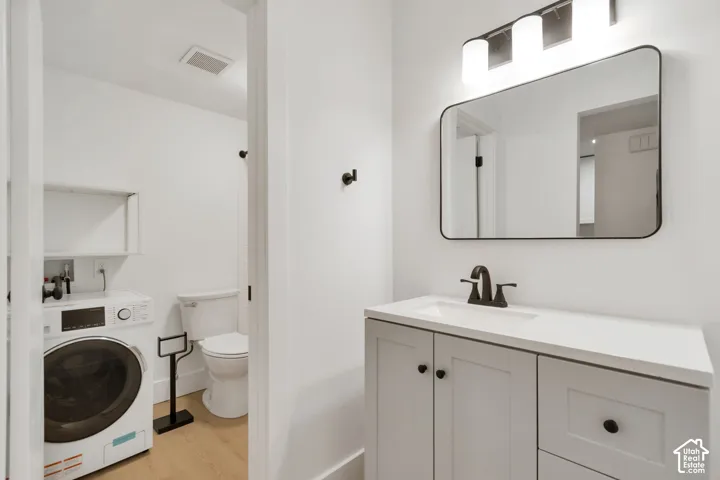 Light gray vanity with a stone countertop, rectangular undermount sink, matte black faucet, and rounded-corner mirror with integrated vanity lighting