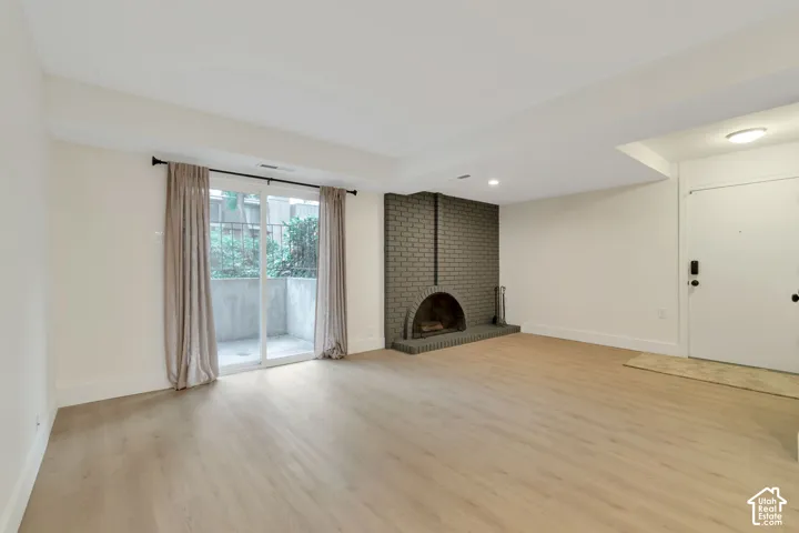 Living space featuring wood-finish flooring, a painted brick fireplace with a rounded hearth, sliding glass doors, and recessed lighting