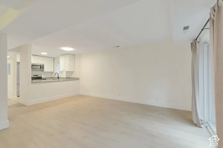Open-concept area featuring light wood-finish flooring, white shaker-style cabinetry, stainless steel appliances, a peninsula countertop, and sliding glass doors