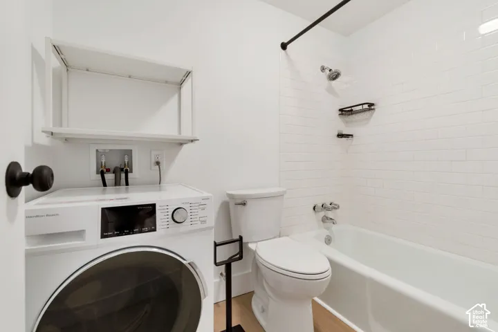 Bathroom featuring a tub with white subway tile surround, matte black shower fixtures, wall-mounted storage shelving, and a toilet