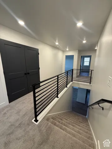 Hallway featuring recessed lighting, charcoal-toned double doors, neutral wall-to-wall carpeting, and a black metal horizontal railing system