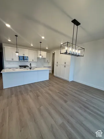 Kitchen featuring white cabinetry, wood-finish flooring, a kitchen island with stone-surface countertop, matte black hardware, and an industrial-style geometric chandelier