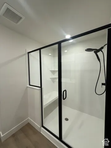 Walk-in shower featuring a matte black frame, glass door, hand-held showerhead, integrated seating, and corner shelving