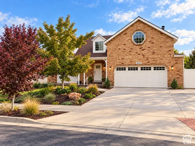 Brick exterior featuring a gabled roofline, an attached three-car garage, an octagonal accent window, and professional landscaping