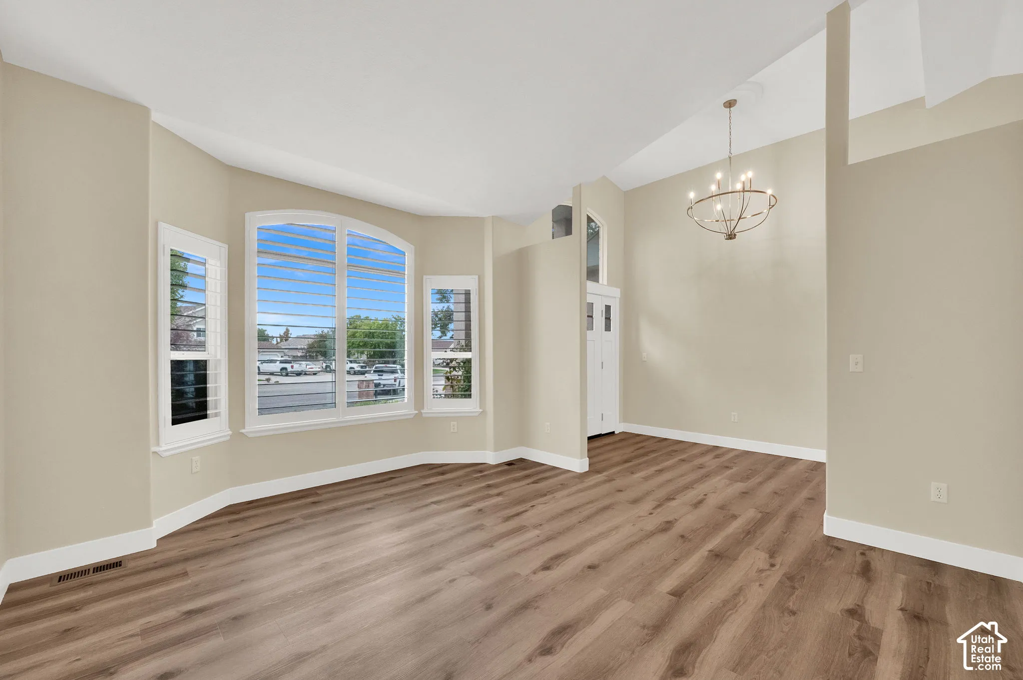 Vaulted ceilings, wood-finish flooring, bay window with arched top detail, and suspended chandelier fixture