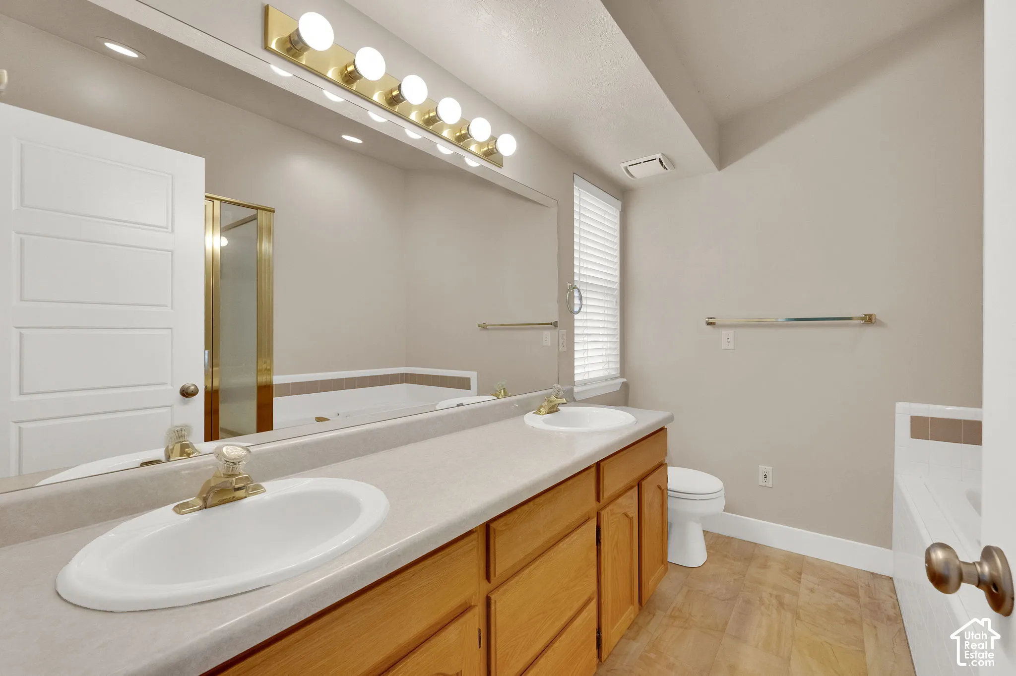 Double vanity featuring oval drop-in sinks, a full-width mirror, wood cabinetry, and a tiered soaker tub