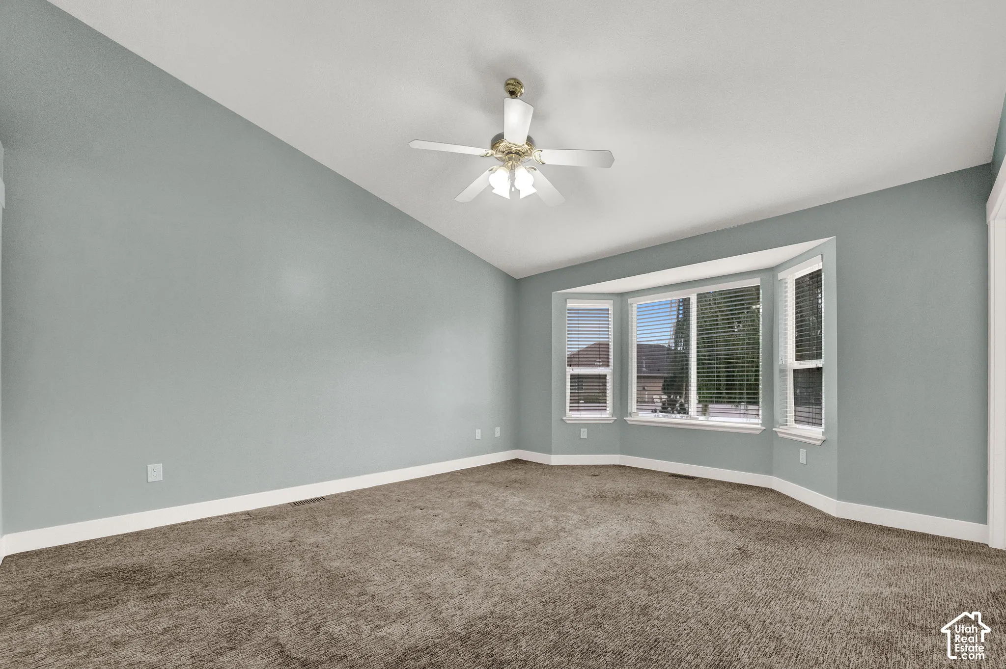 Vaulted ceiling featuring a central multi-blade ceiling fan with integrated lighting and a prominent bay window configuration