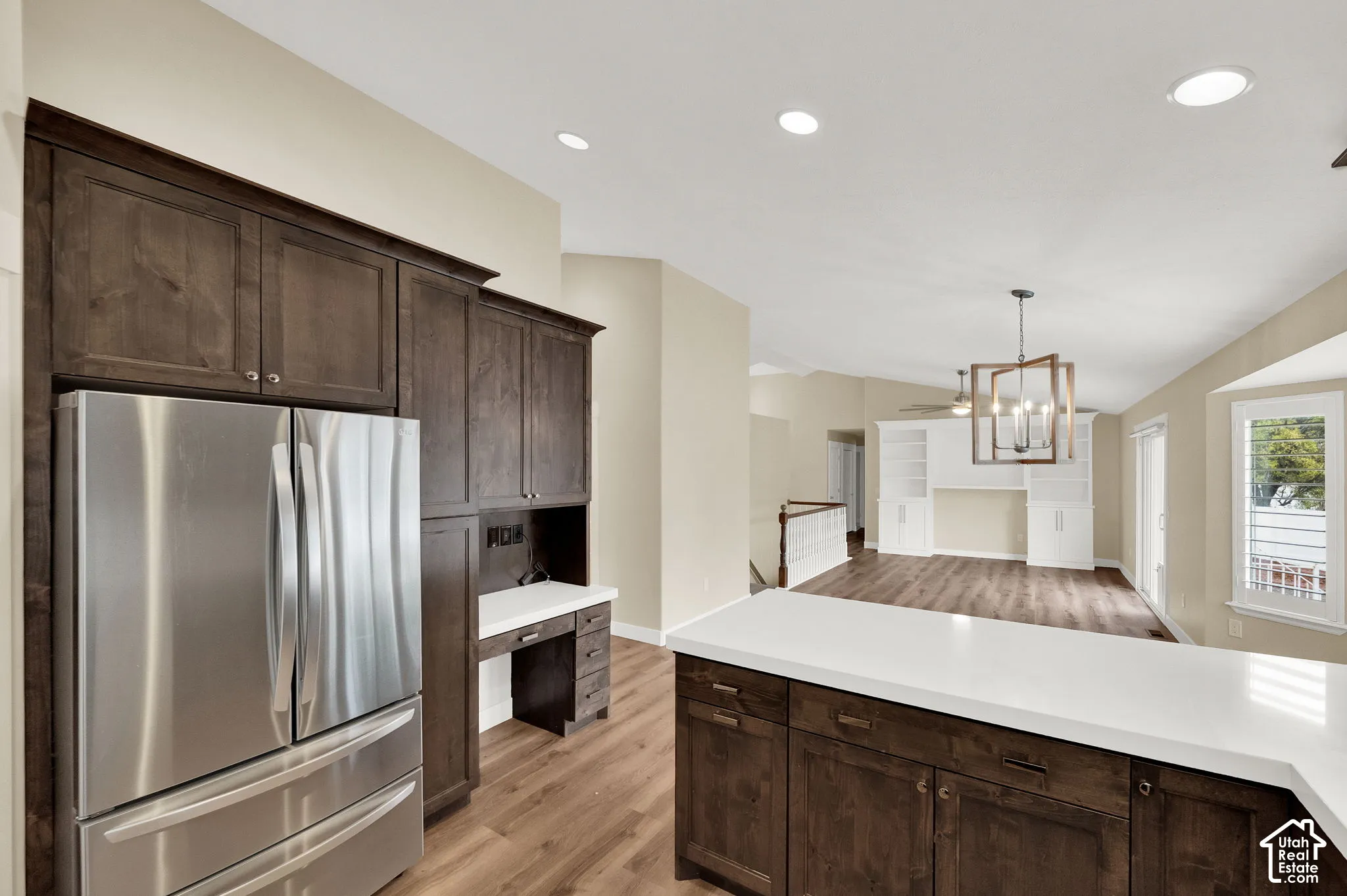 Kitchen featuring dark-stained cabinetry, quartz countertops, a built-in desk, stainless steel refrigerator, and wood-finish flooring