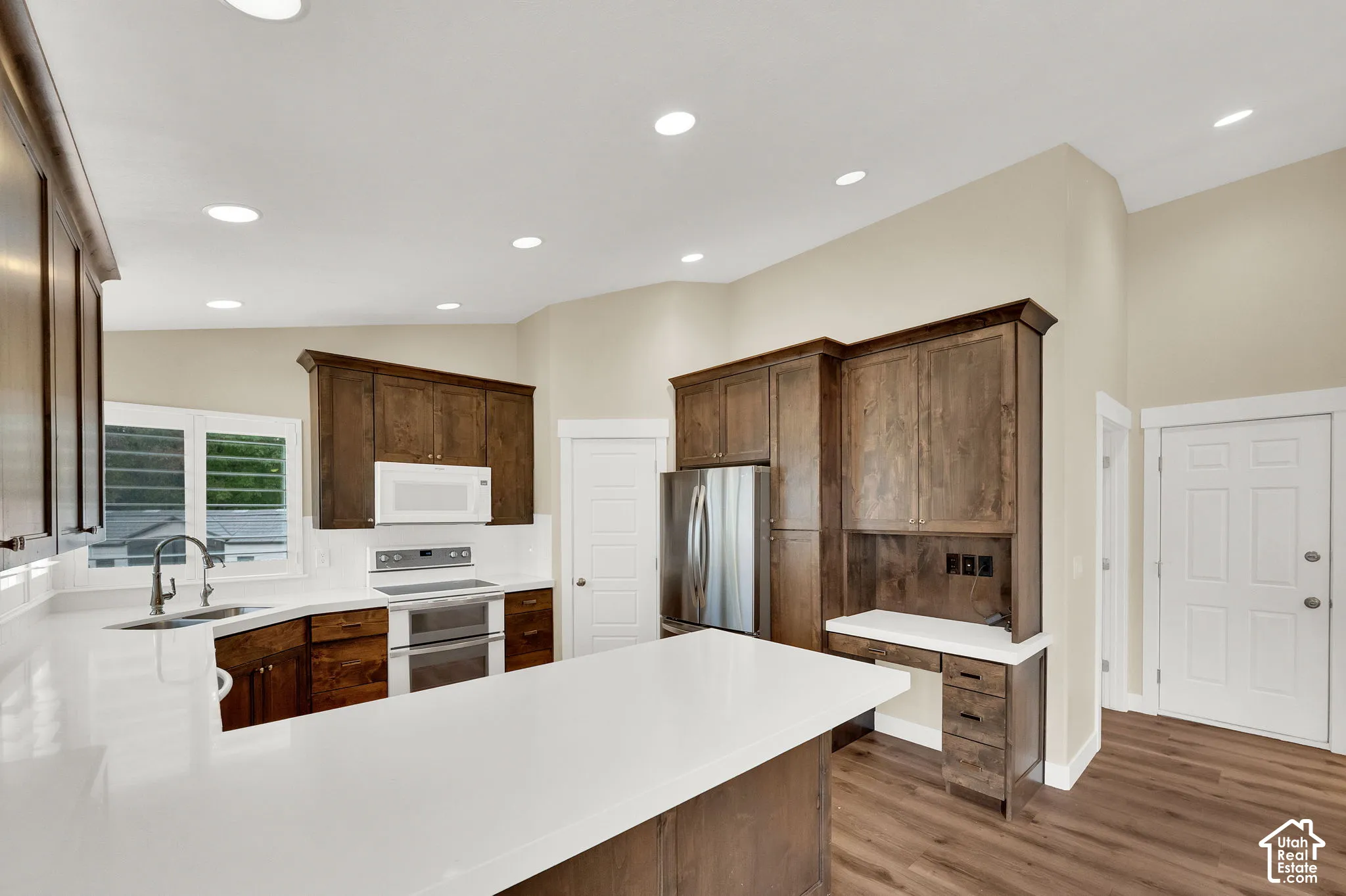 Kitchen featuring dark-stained wood cabinetry, white countertops, stainless steel appliances, a built-in workspace, and wood-finish flooring