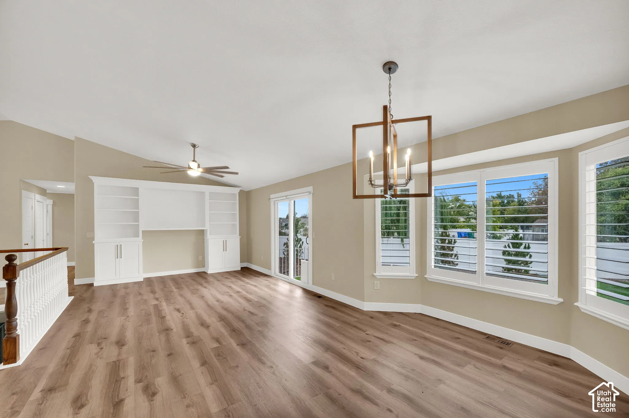 Wood-finish flooring, built-in white cabinetry, geometric pendant lighting, sliding glass door, and bay window featuring plantation shutters