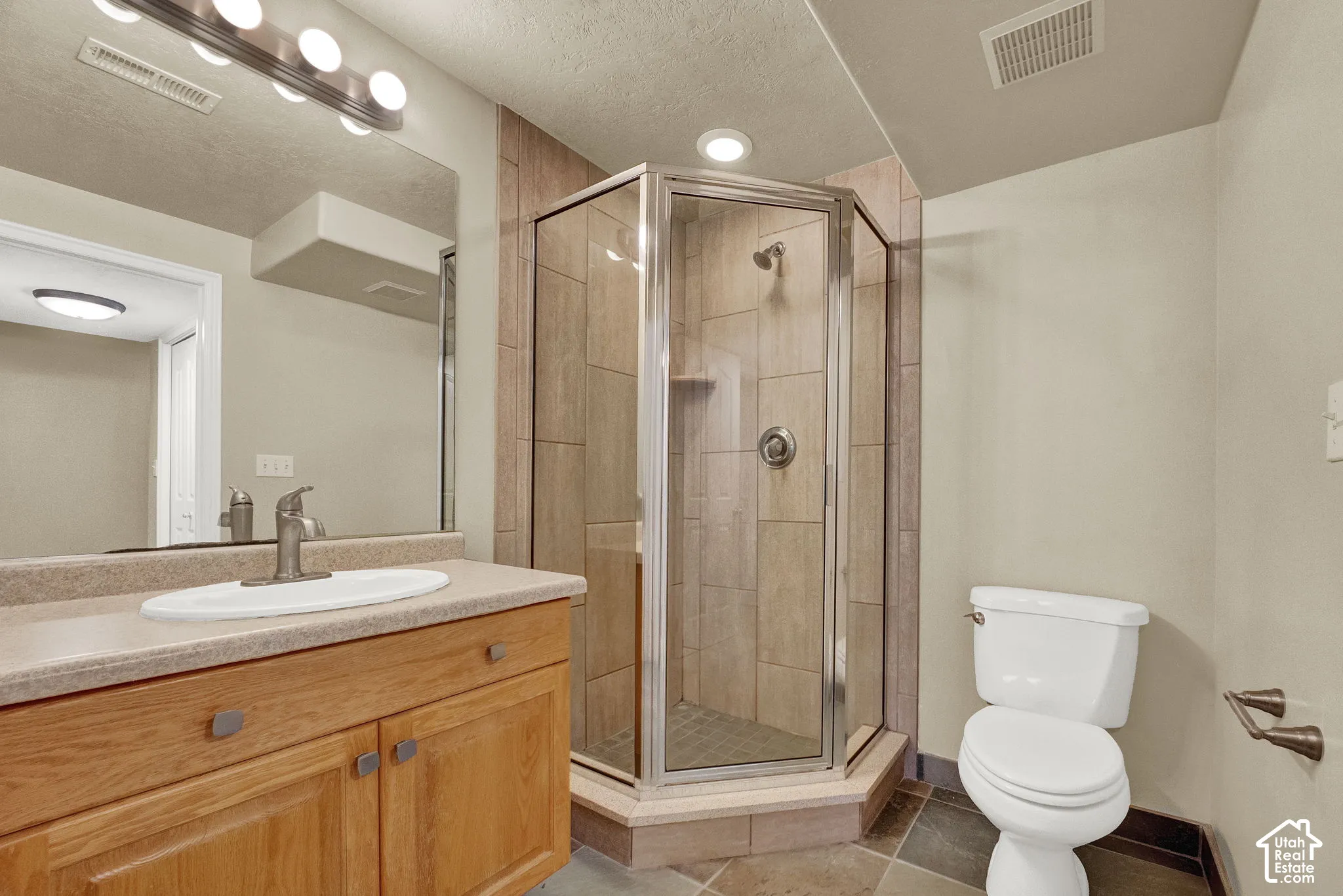 Wood vanity featuring a solid surface countertop with an integrated basin, corner glass-enclosed shower with tile surround, and tile flooring